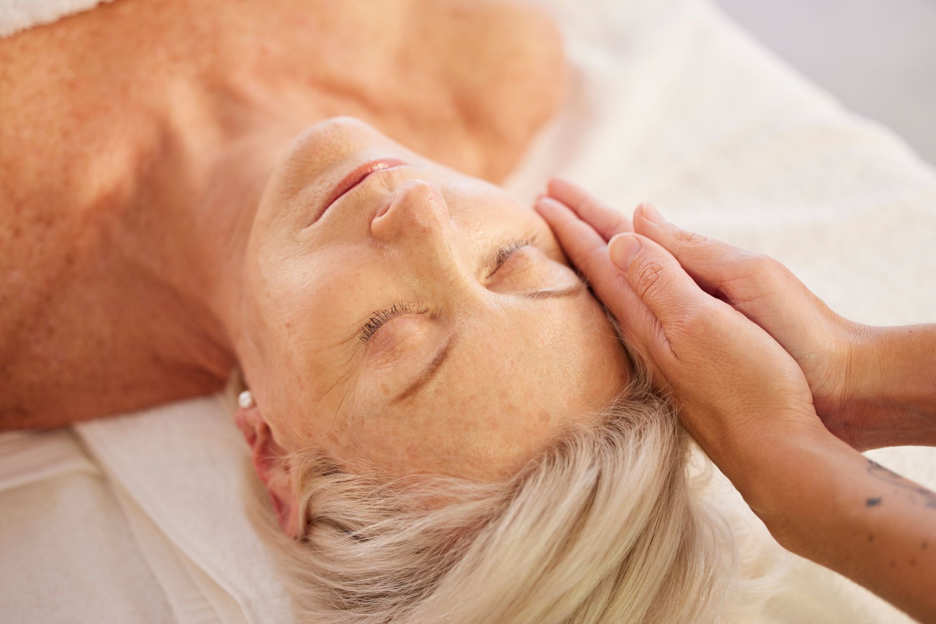 Woman receiving a facial massage with eyes closed, lying on a spa treatment table