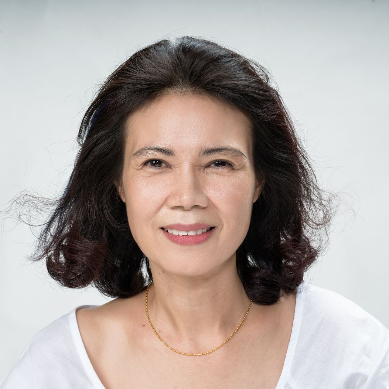 A woman wearing a white shirt and a gold necklace is smiling for the camera.