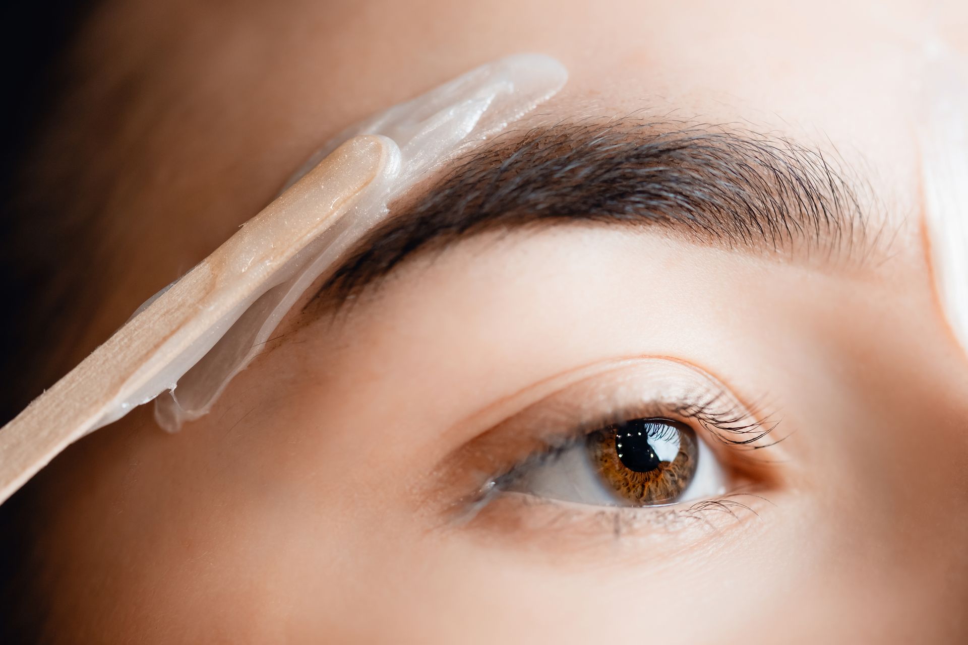 A woman is waxing her eyebrows with a wooden stick.