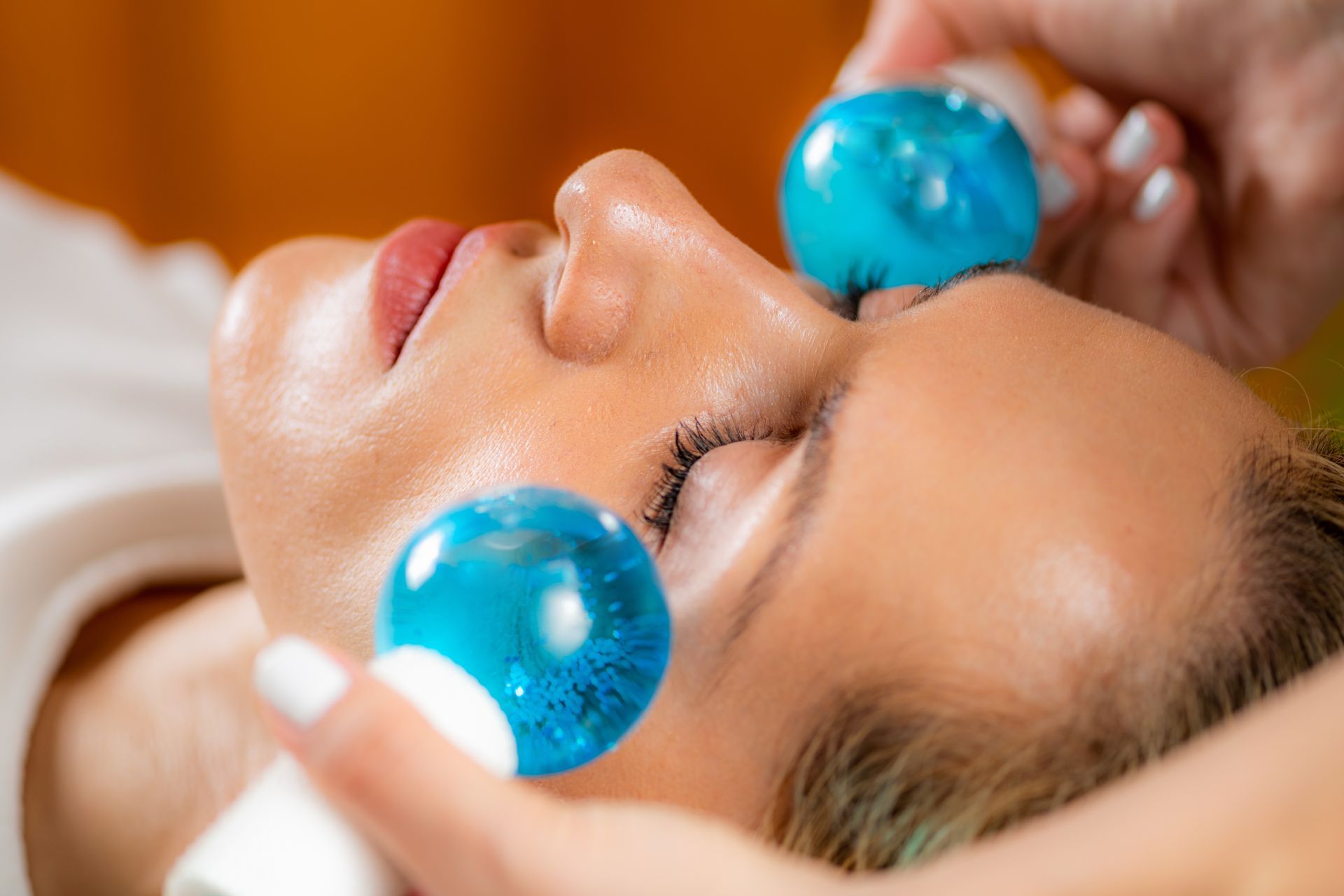 A woman is getting a facial treatment with blue ice balls on her face.