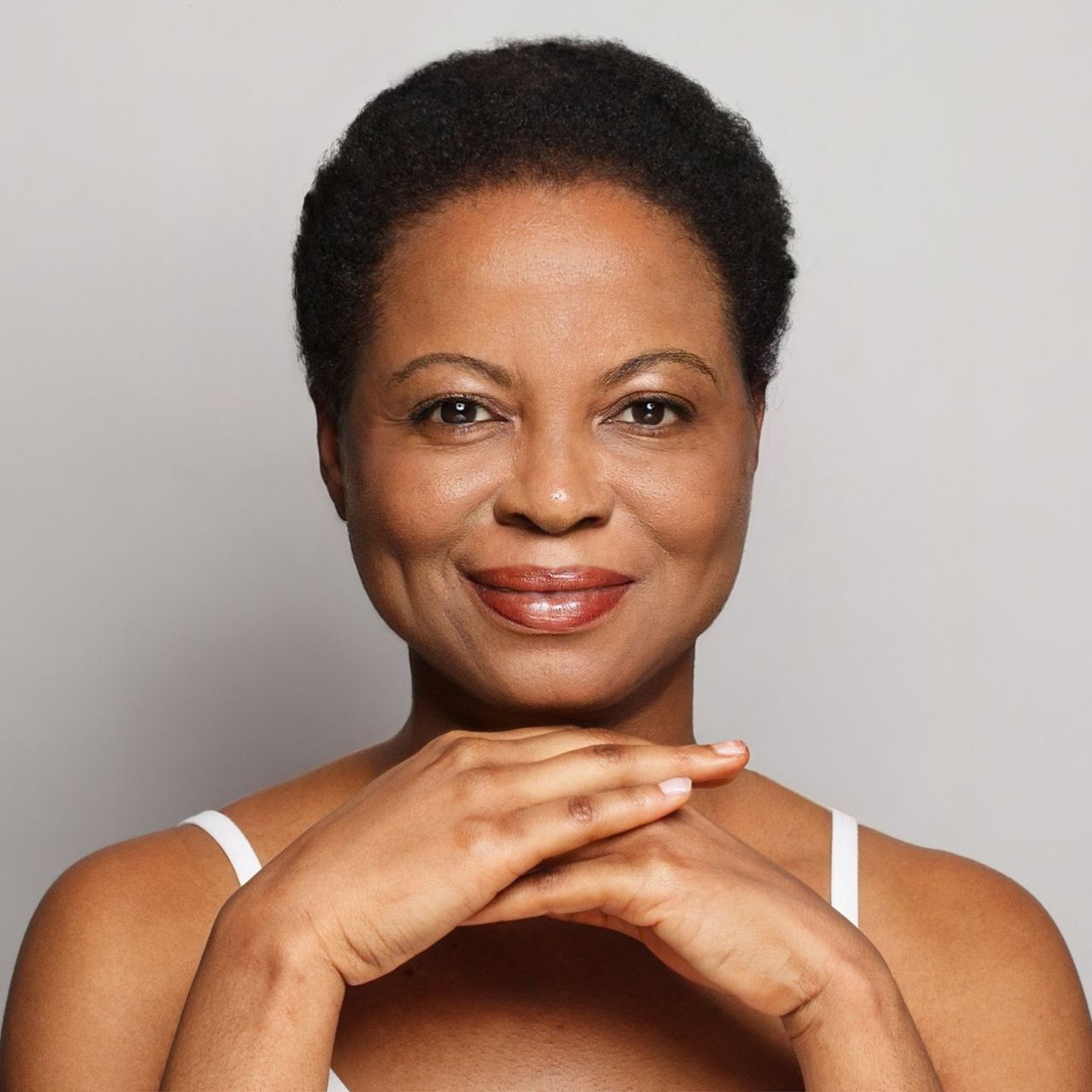 A woman is smiling with her hands folded on her chin