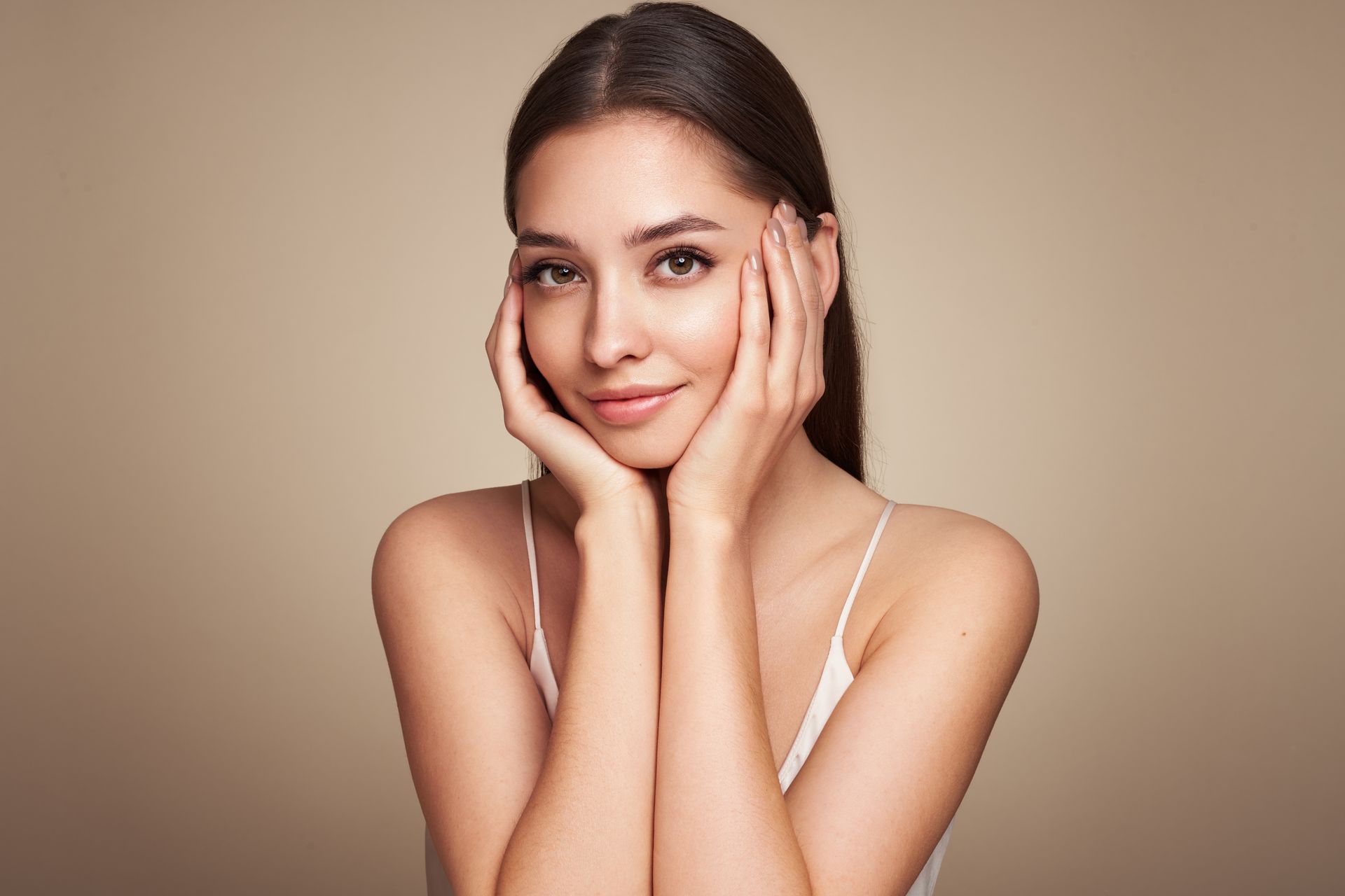 A woman is touching her face with her hands and smiling.