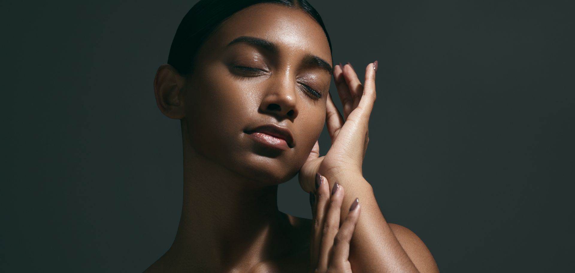 A woman is posing with her eyes closed and her hand on her face.