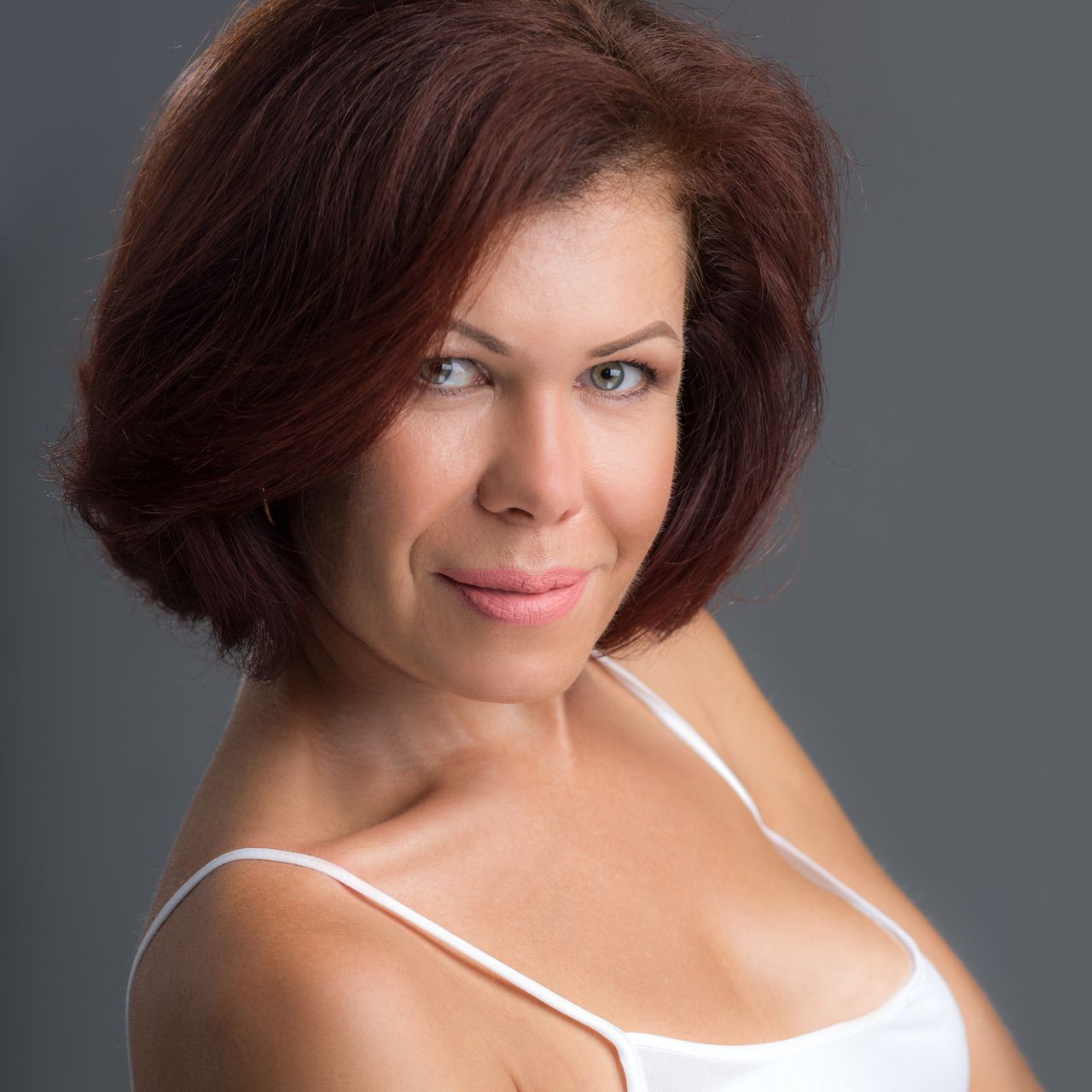 A woman with short red hair is wearing a white tank top