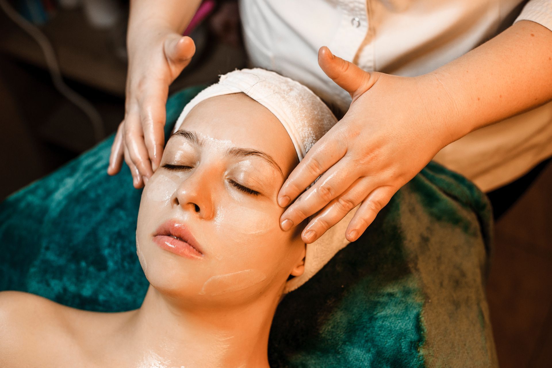 Person receiving a facial massage with cream applied to the face; hands on the forehead and cheeks.