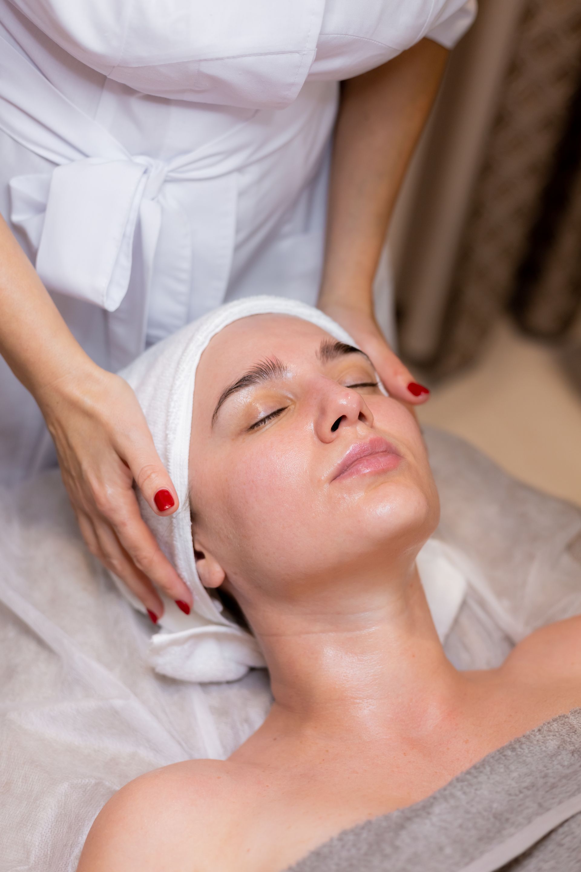 Spa therapist giving a facial massage to a client lying with eyes closed and a towel headband