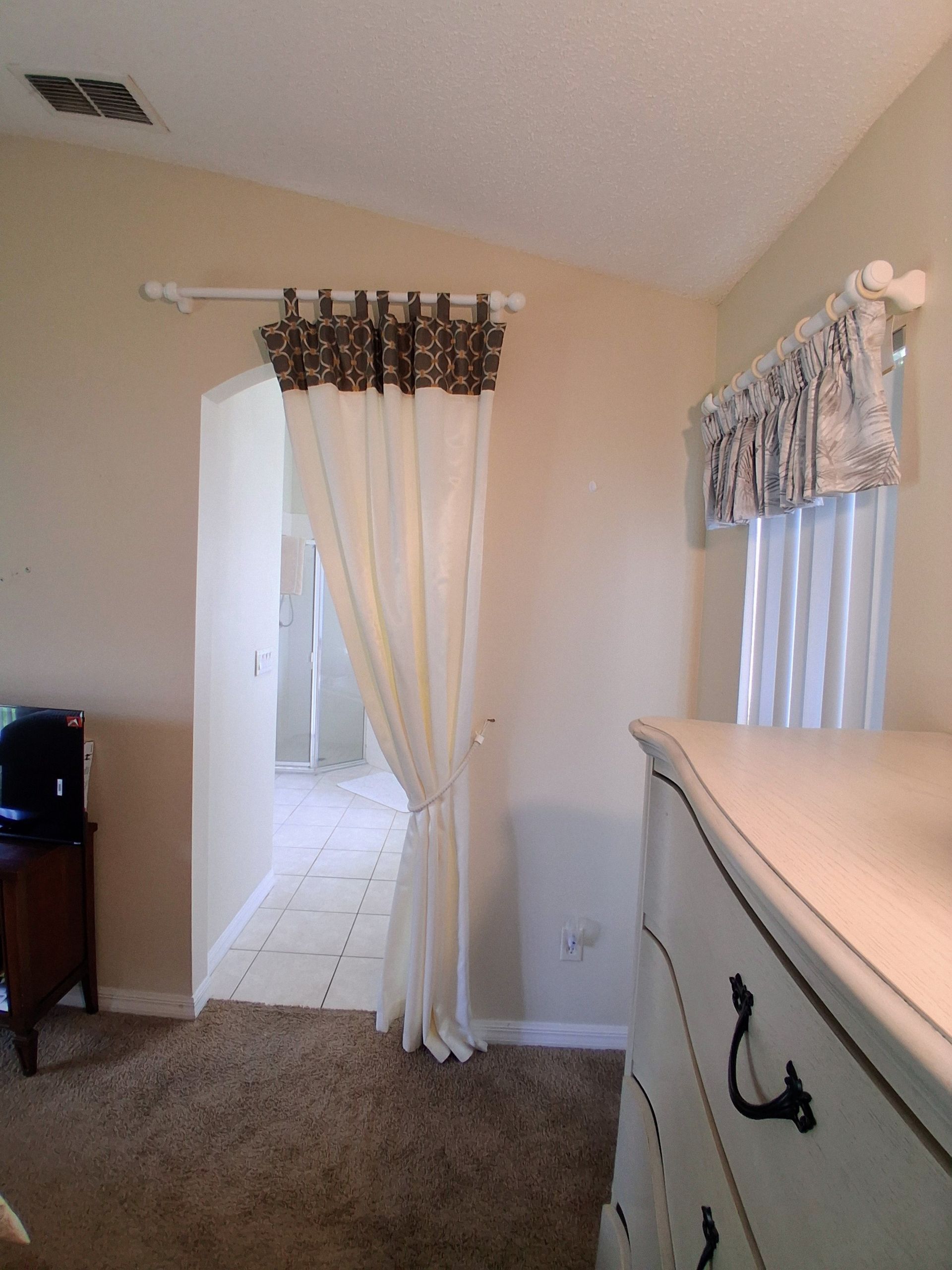Small room with beige carpet, curtained doorway, and white dresser beside a window.