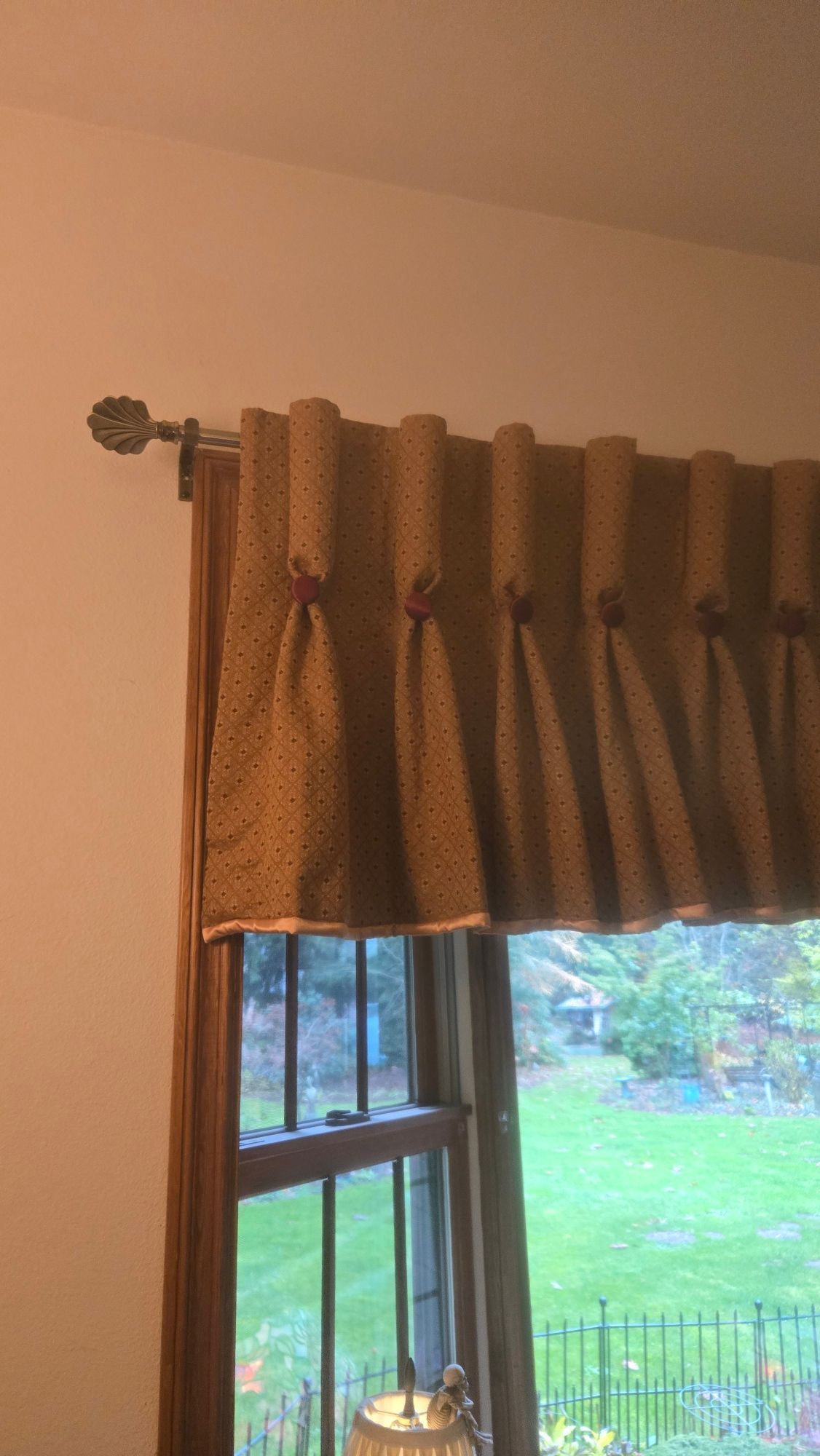 Tan curtains with grommets beside a window showing a green backyard outside