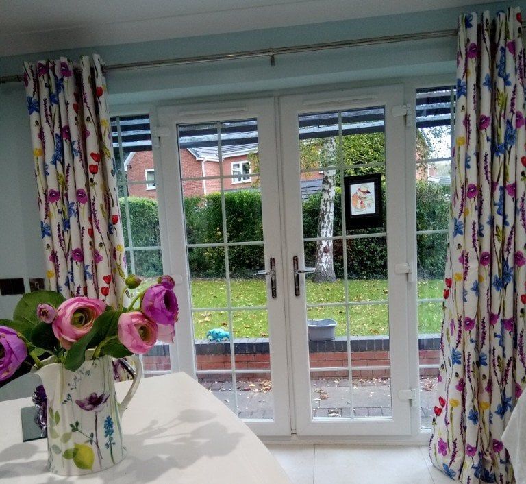 Bright room with French doors, floral curtains, and a vase of pink flowers on a table