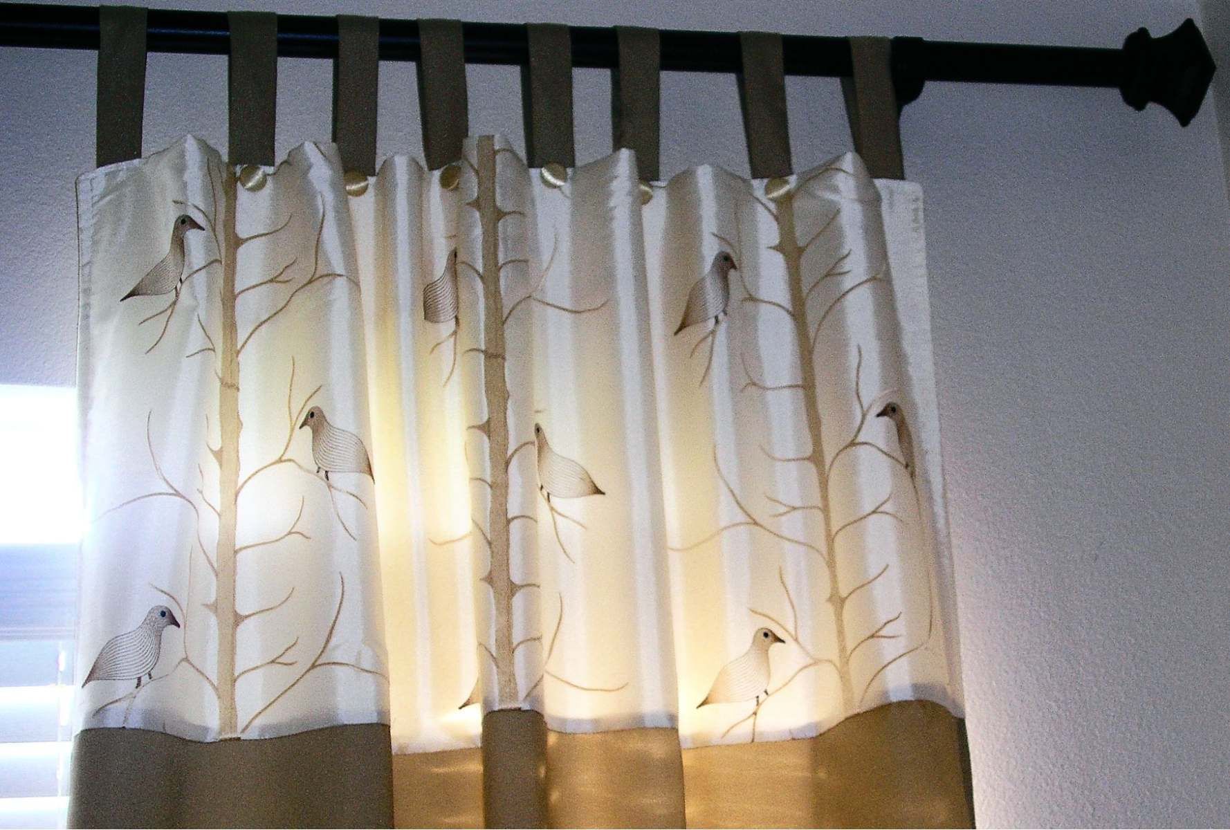 Sheer white curtains with leaf pattern hanging in front of a sunlit window
