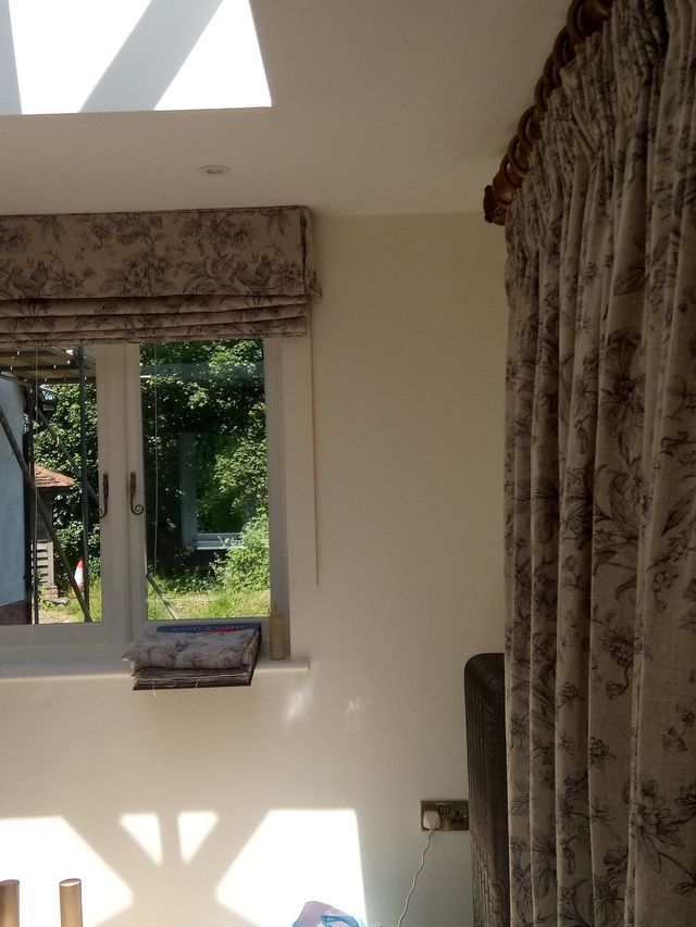 Sunlit room with a window, patterned curtains, and a wall-mounted shelf overlooking greenery outside