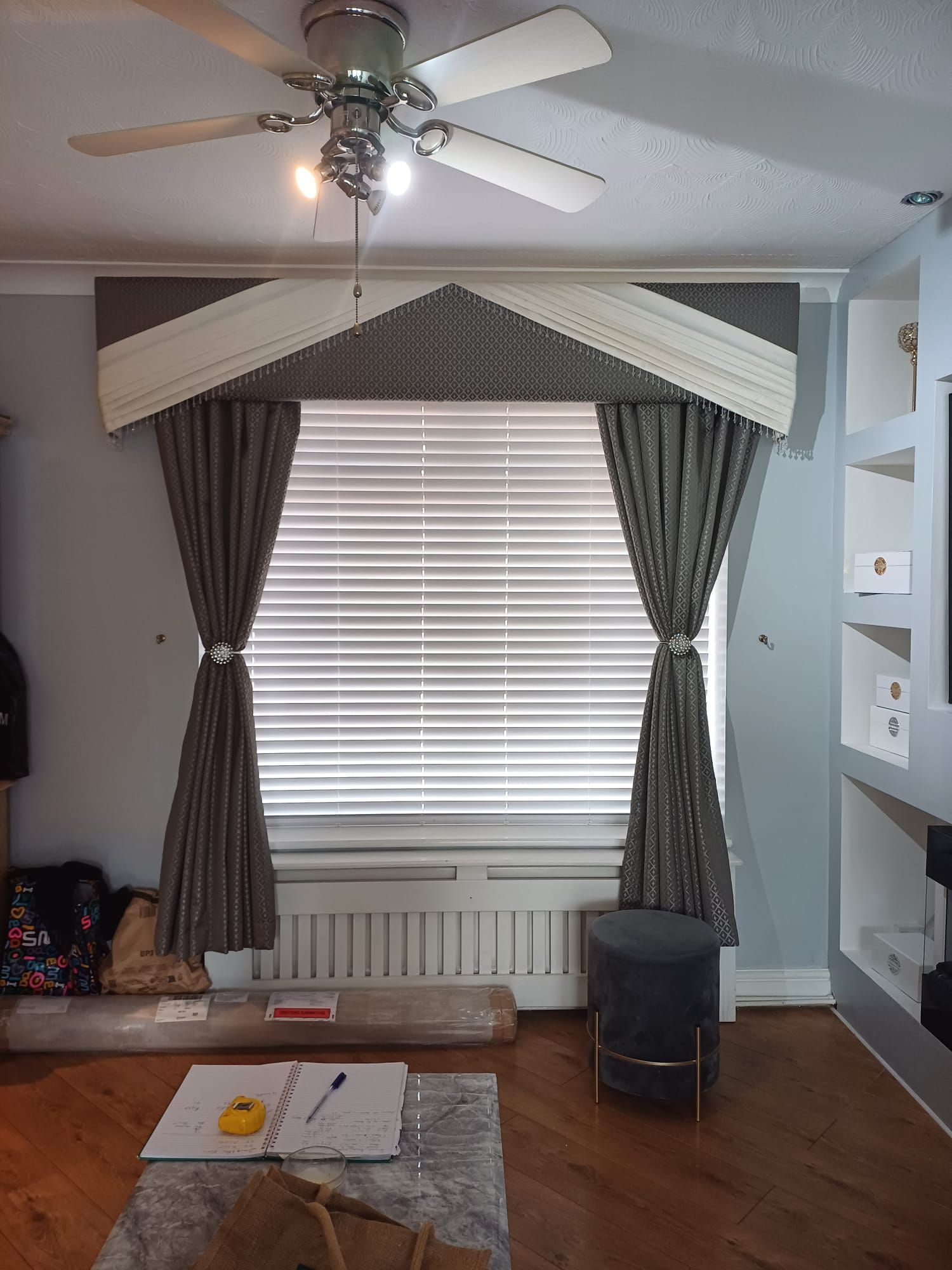 Living room window with dark curtains, white blinds, ceiling fan, and a radiator below.