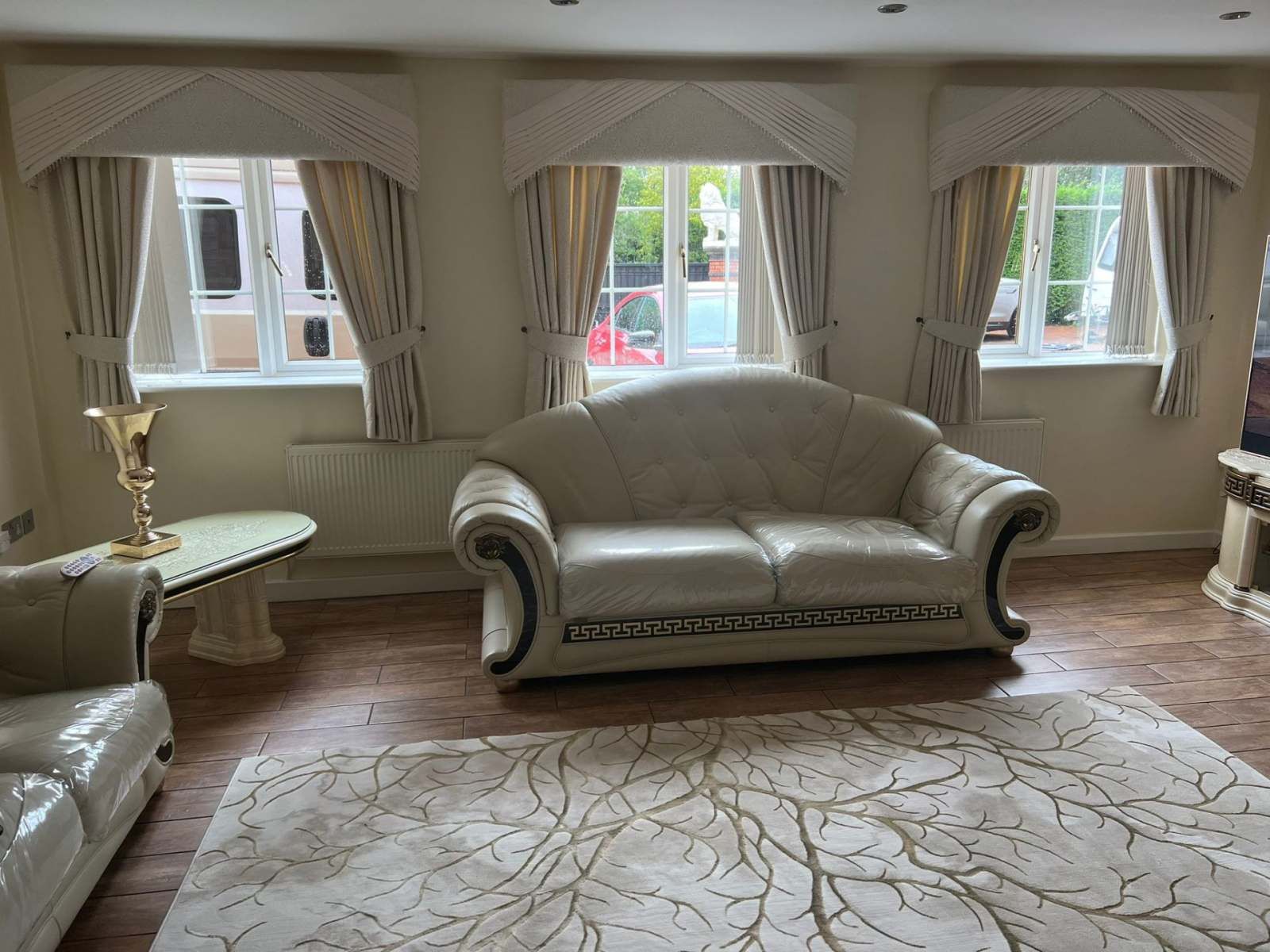 Elegant living room with beige sofa, patterned rug, and three windows with drapes and daylight