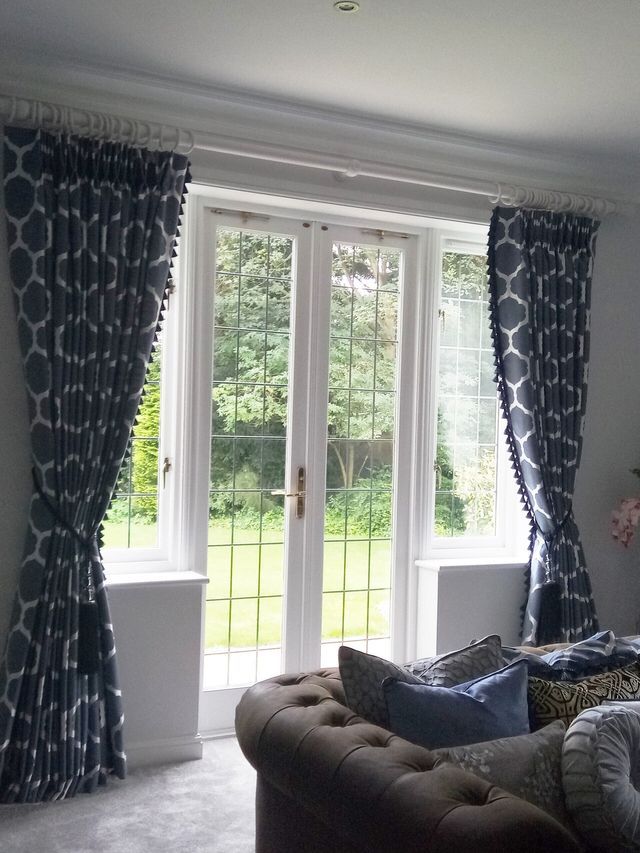 Living room with white French doors, dark patterned curtains, and a sofa facing a green garden outside