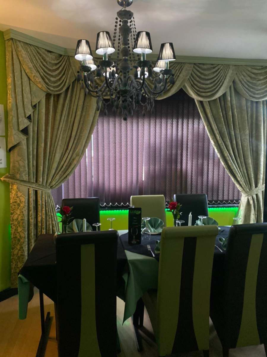 Elegant dining room with draped curtains, chandelier, and a set dining table with green-backed chairs.