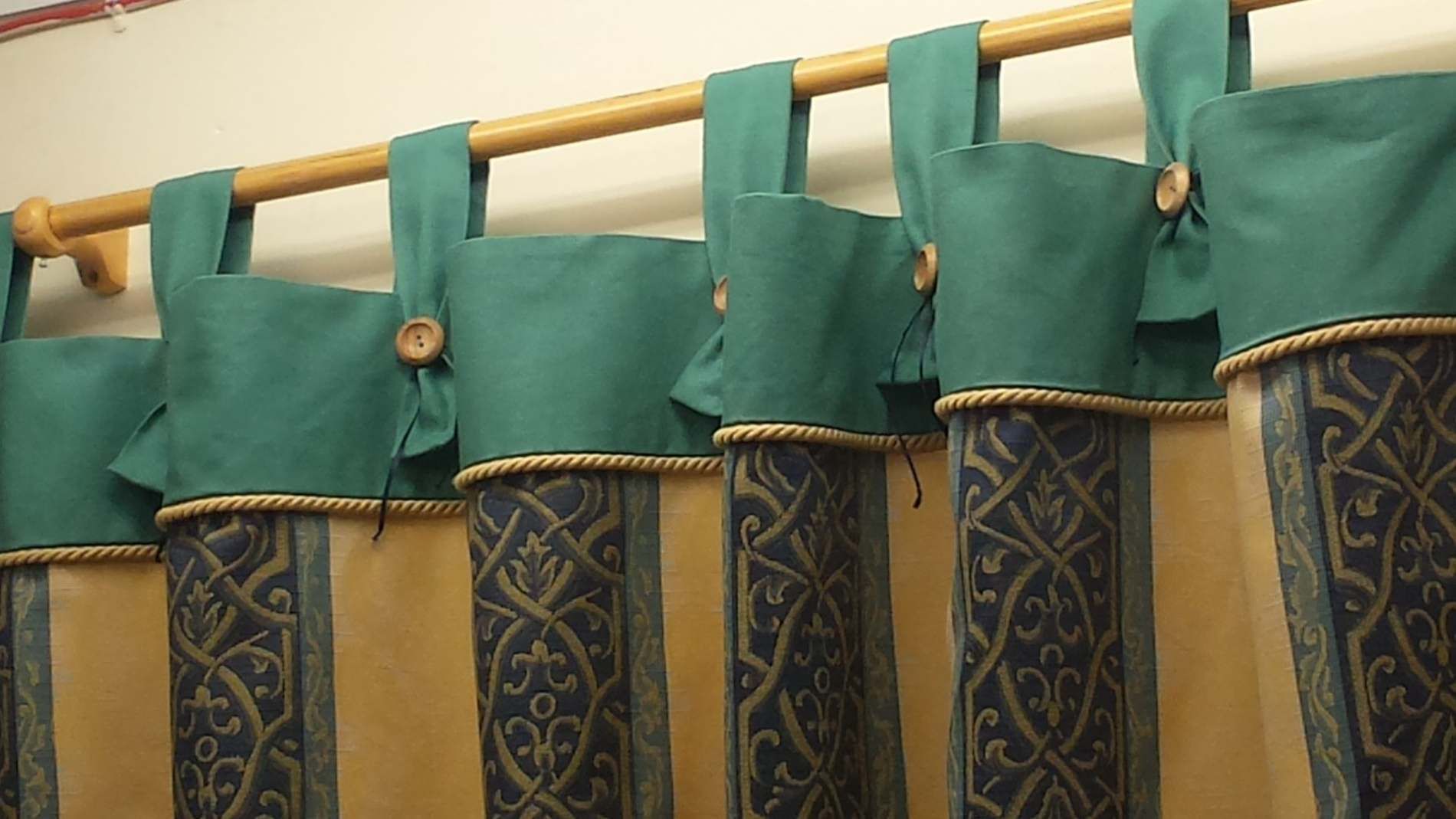 Green fabric shower curtains hanging on a gold rod, with blue-and-gold patterned panels below.