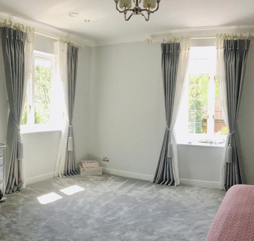Bright empty living room with gray carpet, white walls, tall windows, and gray curtains.