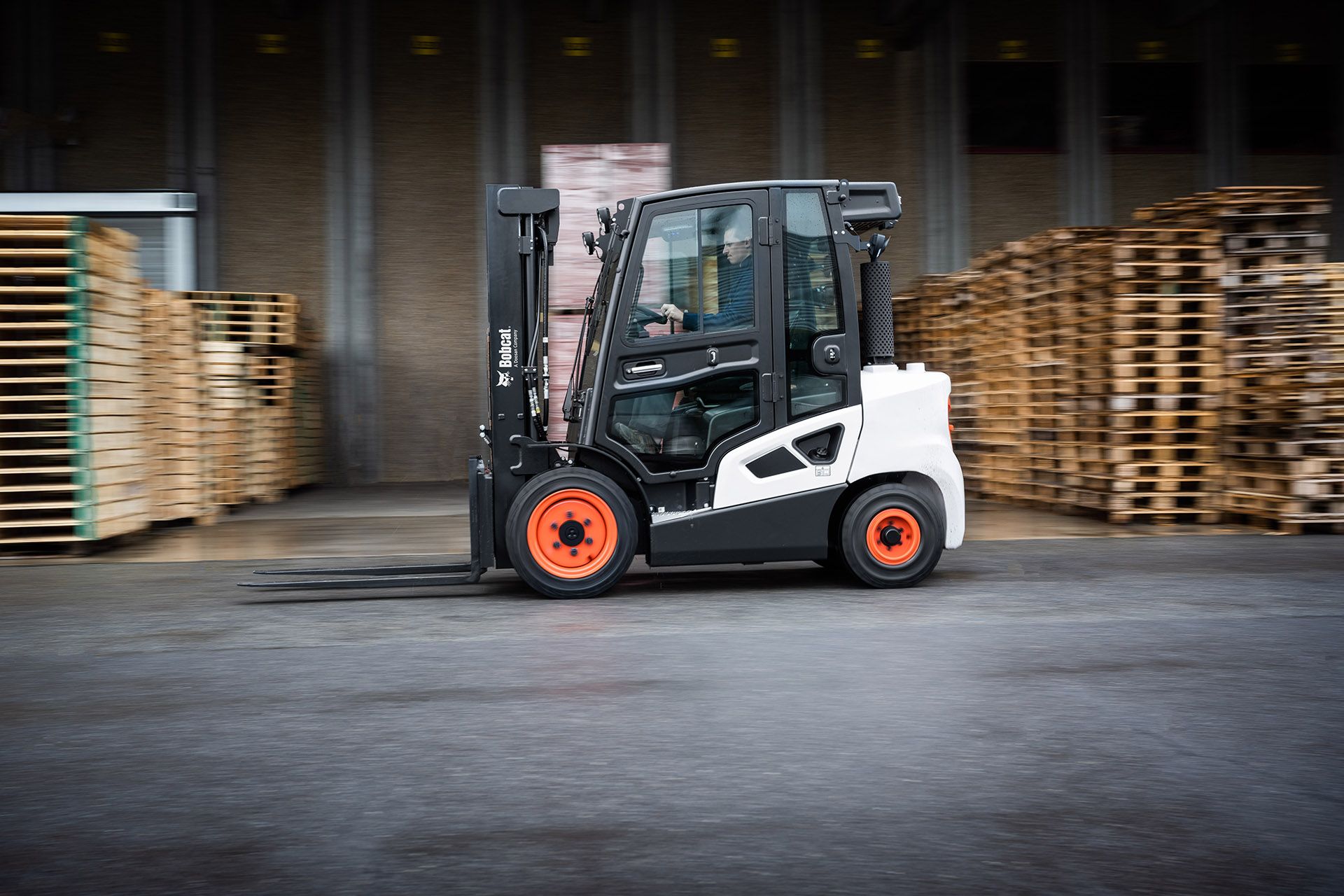 A forklift is driving through a warehouse filled with wooden pallets.