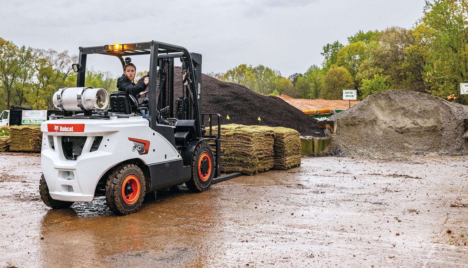 A man is driving a forklift in a muddy field.
