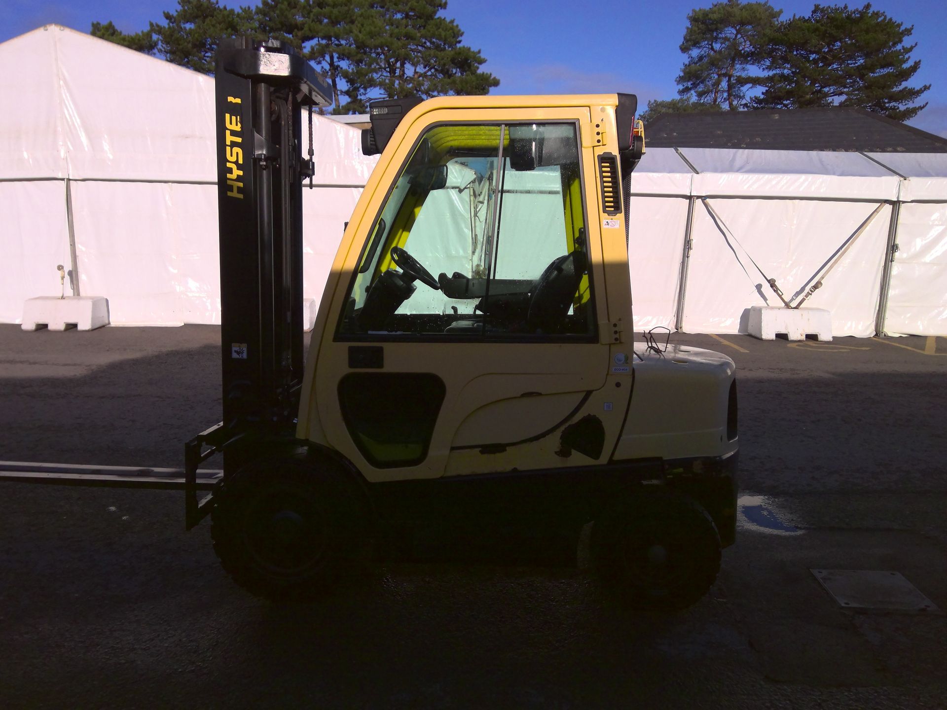 A yellow forklift is parked in front of a fence.
