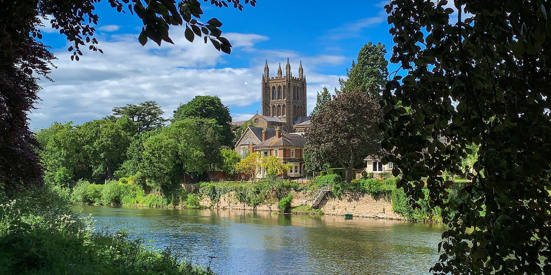 Hereford Cathedral surrounded by trees and the river running along the front