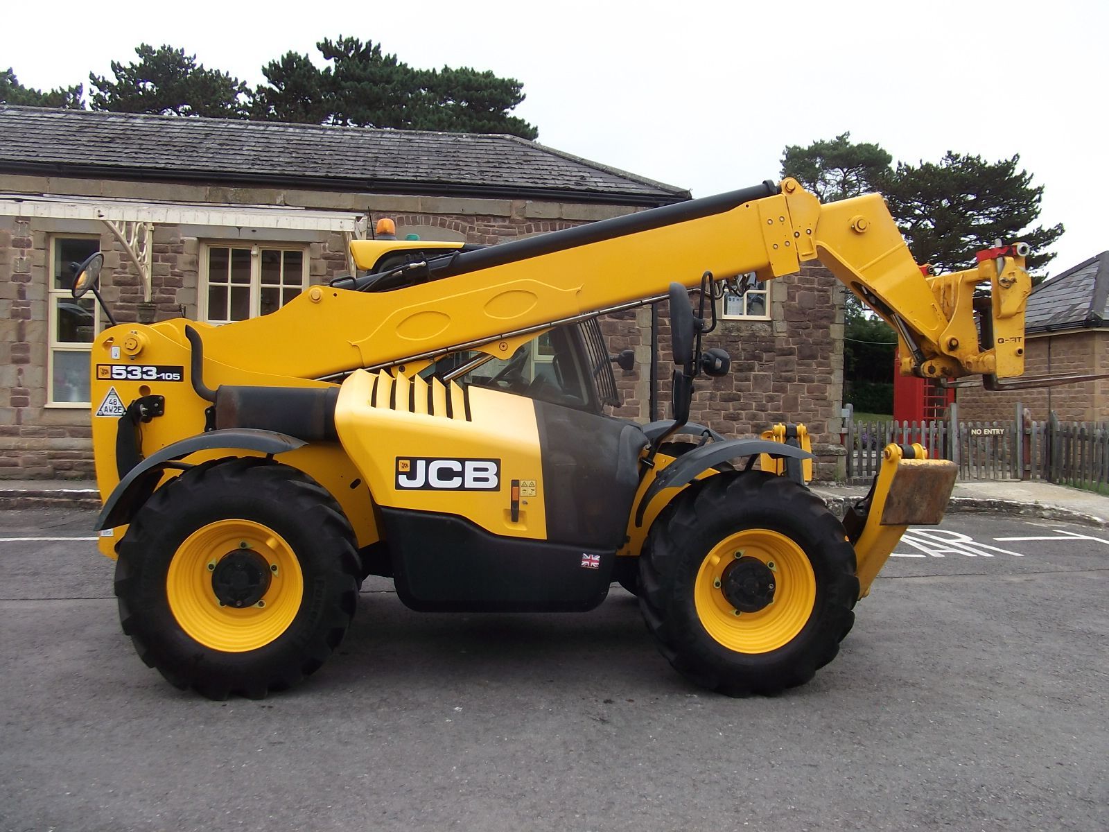 A yellow jcb forklift is parked in front of a brick building