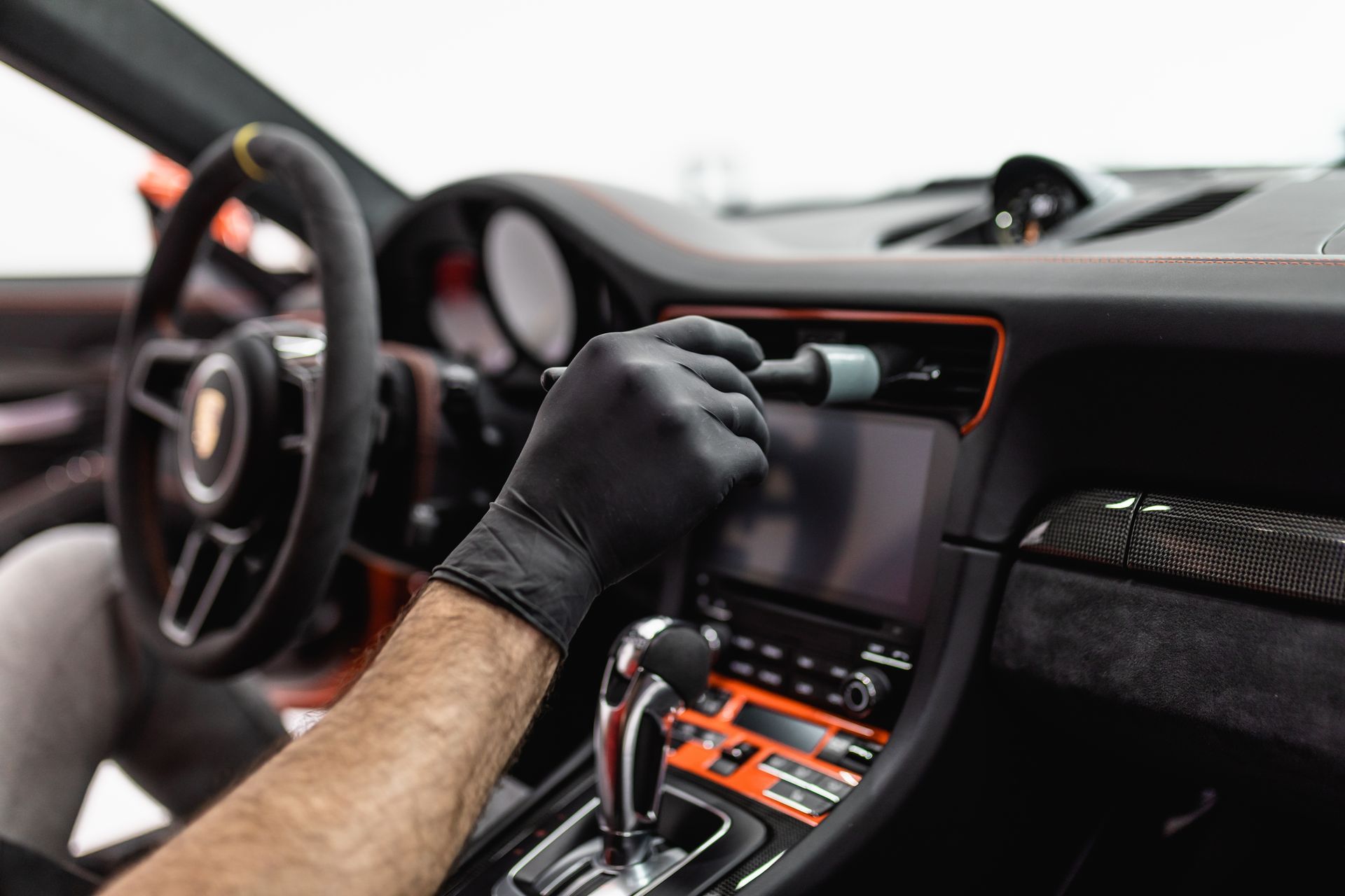 Gloved hand cleaning a car dashboard touchscreen with a cloth inside a vehicle