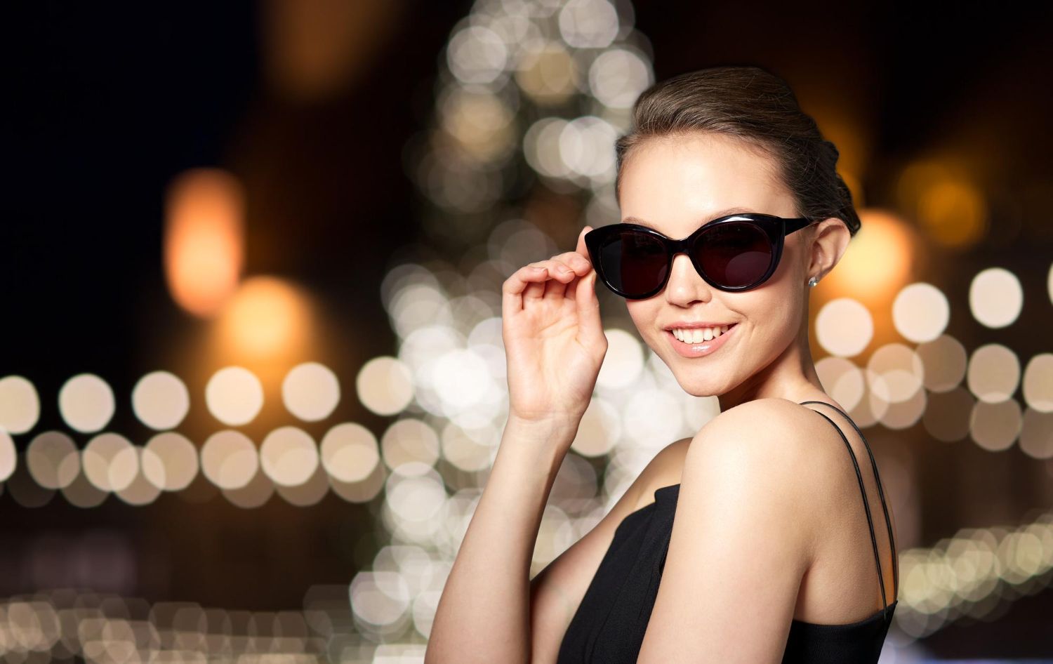 A woman wearing sunglasses and a black dress is standing in front of a christmas tree.