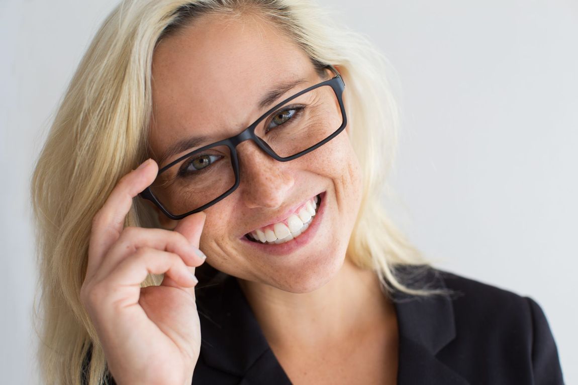 A woman wearing glasses and a black jacket is smiling.