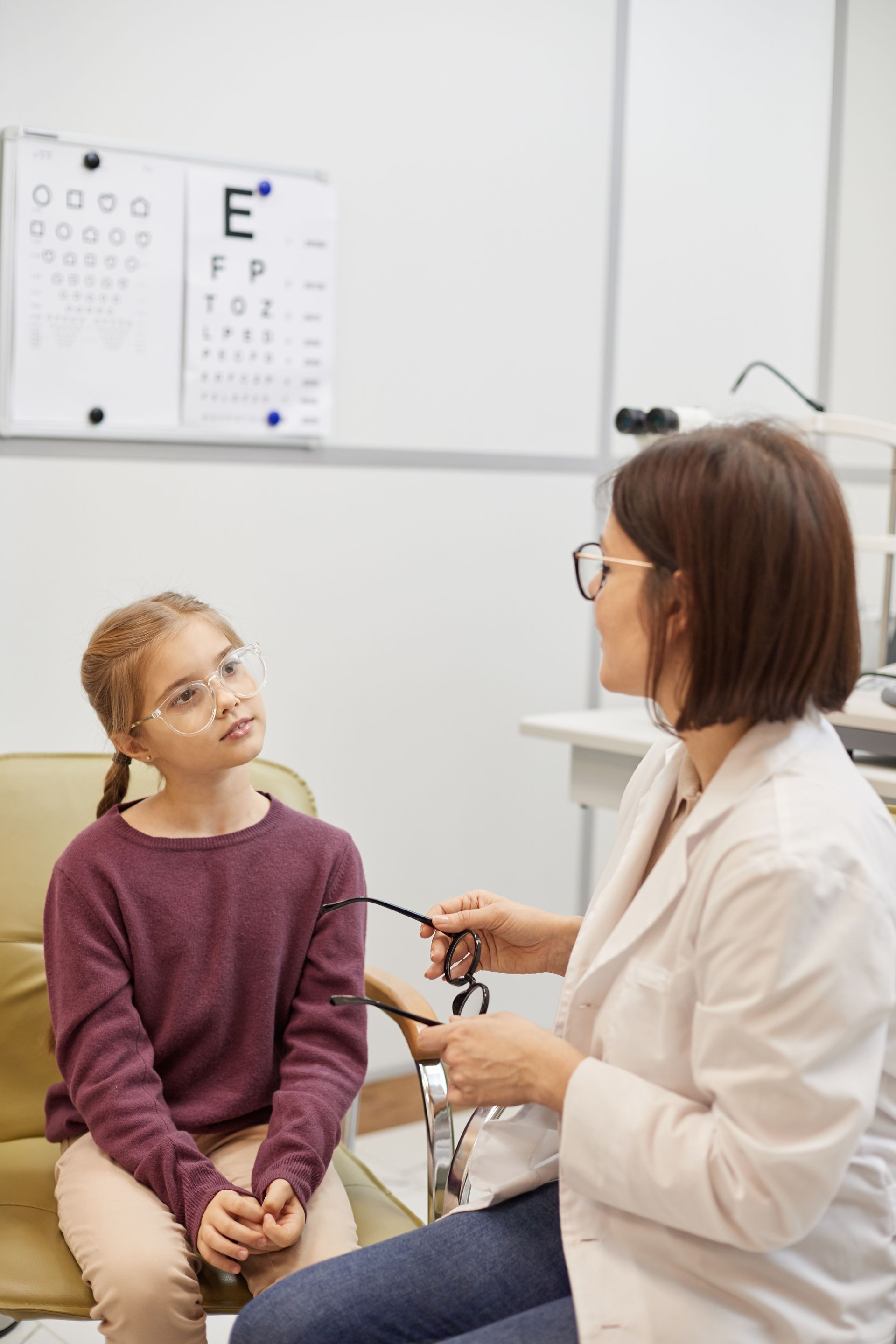 A young boy wearing glasses is standing in front of an eye chart.