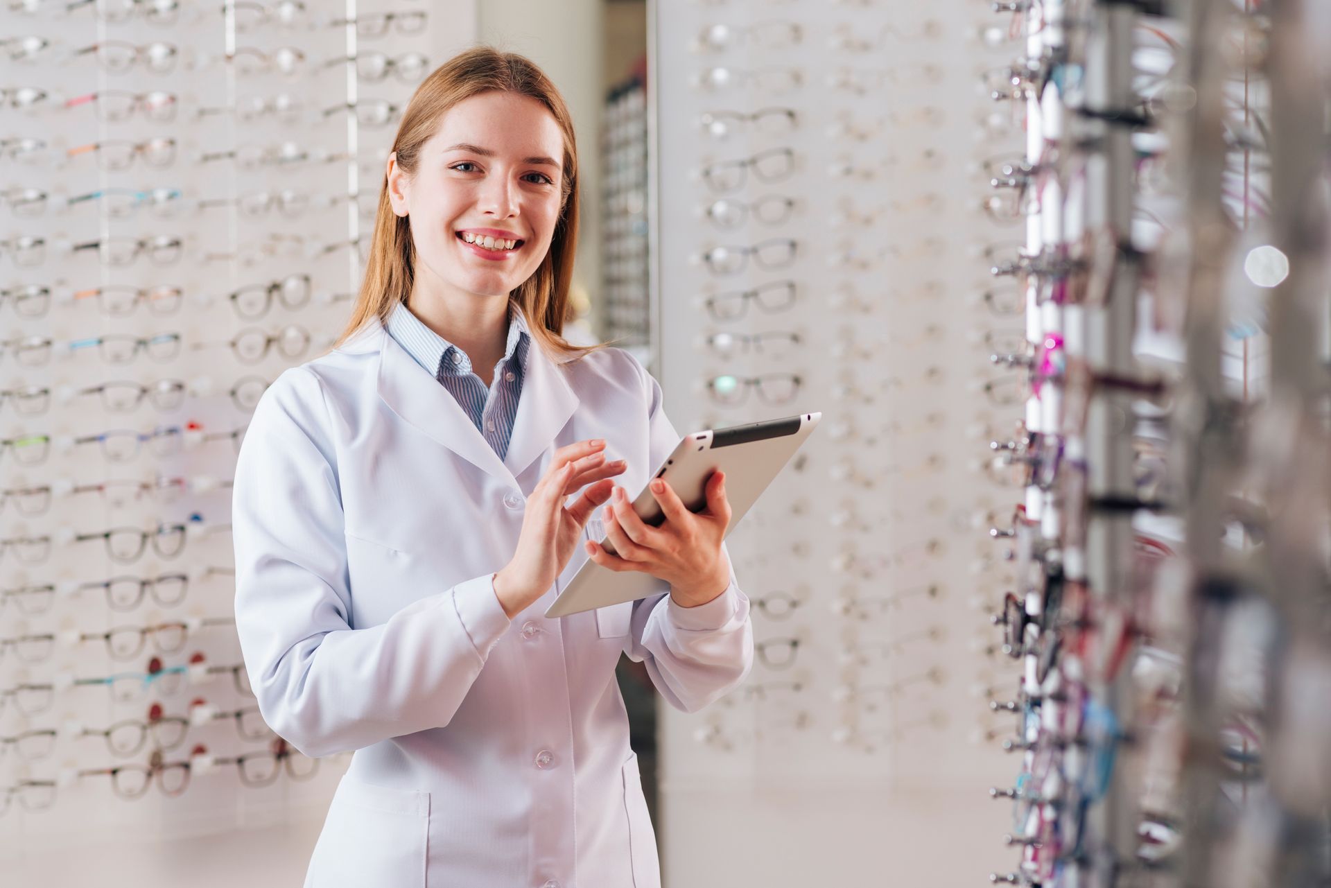 A female optician is holding a tablet in an optical shop.