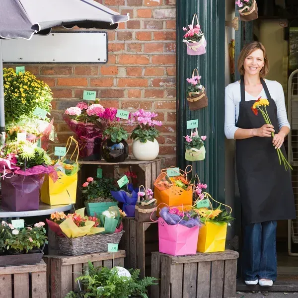 A woman in an apron is standing in front of a flower shop