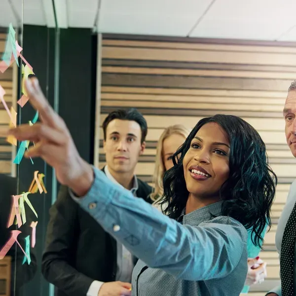 A woman is pointing at a bunch of sticky notes on a wall.