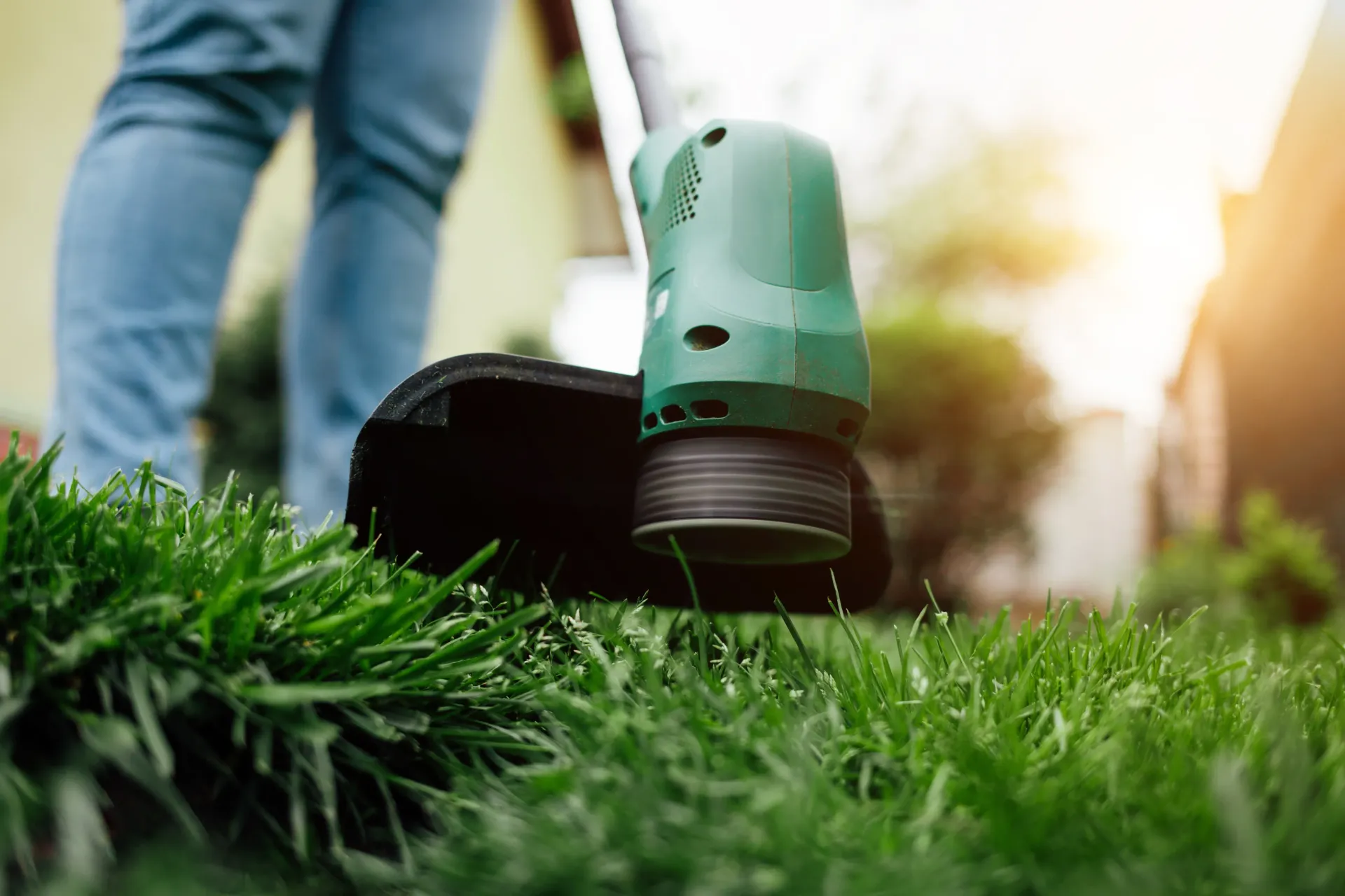Person using a green string trimmer on a lawn.