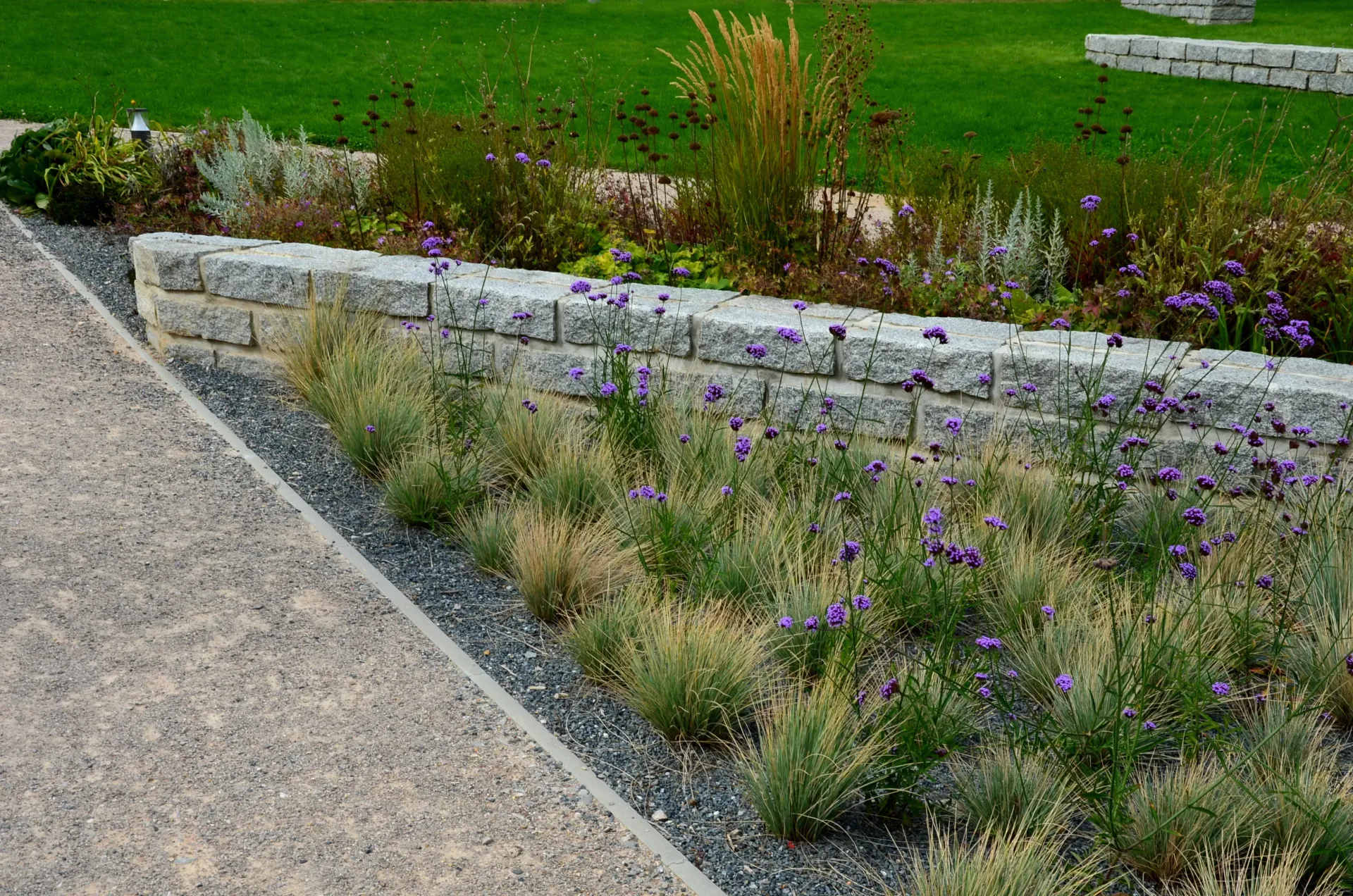 Stone retaining wall with colorful plants and path, a landscape design.