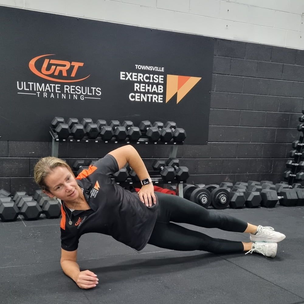 A Woman Is Doing A Side Plank In Front Of A Sign That Says Ultimate Results Training — Ultimate Results Training in Aitkenvale, QLD