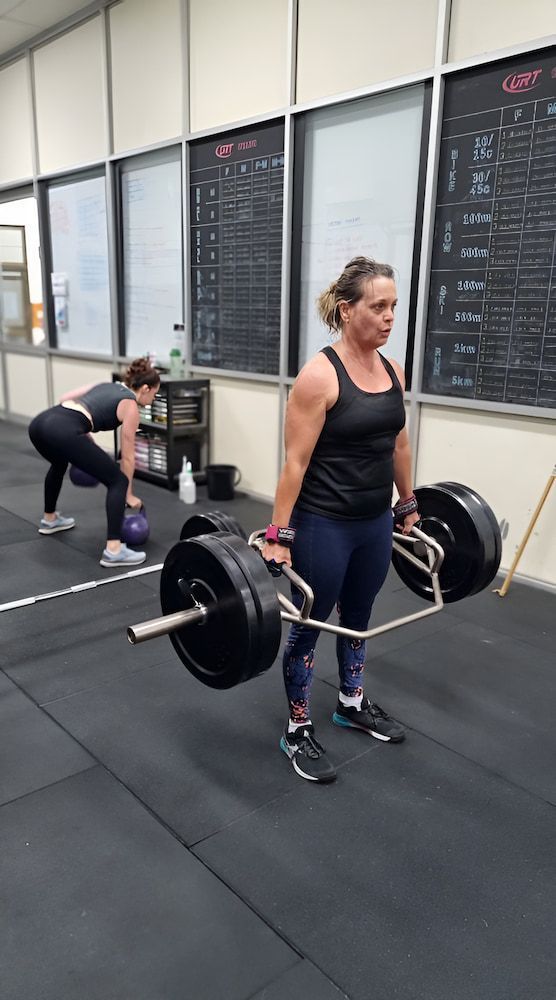 A Woman Is Lifting A Barbell In A Gym — Ultimate Results Training in Aitkenvale, QLD