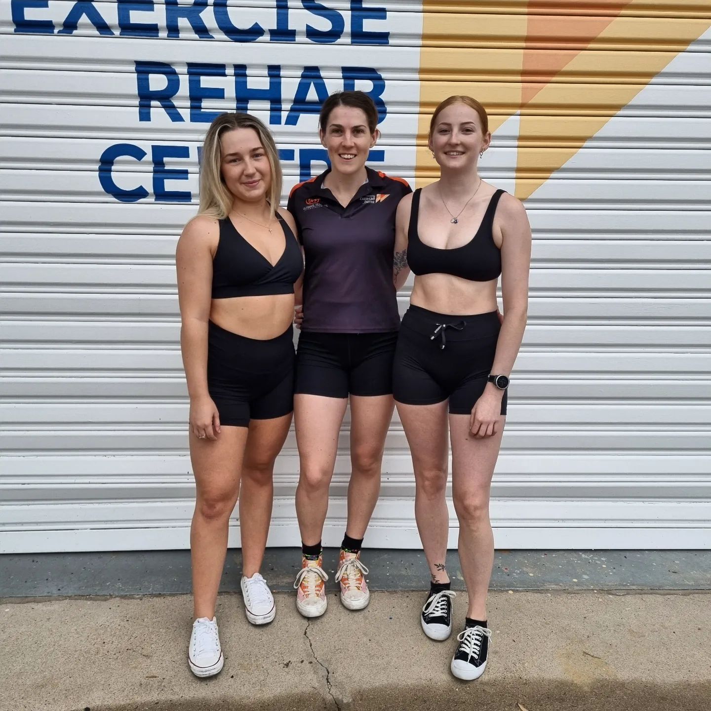 Three People Standing In Front Of A Sign That Says Townsville Exercise Rehab — Ultimate Results Training in Aitkenvale, QLD