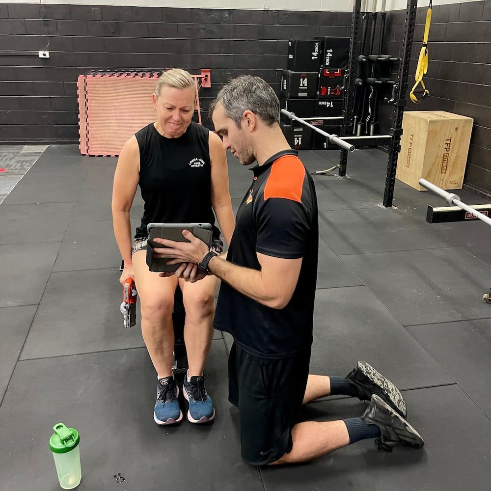 A Man And A Woman Are Kneeling Down In A Gym Looking At A Tablet — Ultimate Results Training in Aitkenvale, QLD