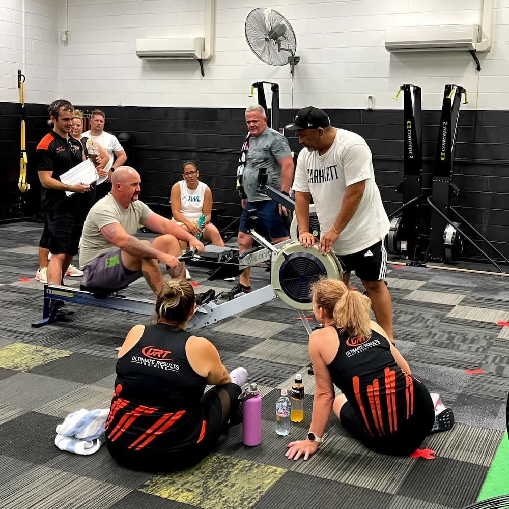 People Are Sitting Around A Rowing Machine In A Gym — Ultimate Results Training in Aitkenvale, QLD