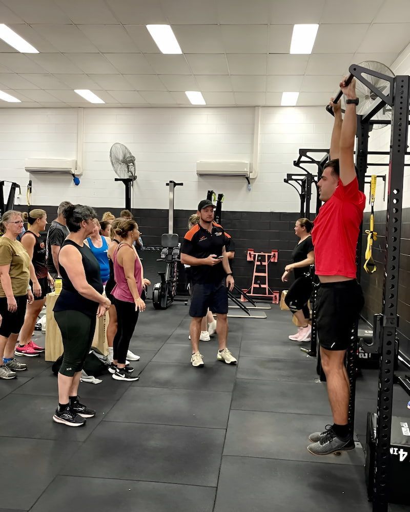 People Are Standing In A Gym Watching A Man Do Pull Ups — Ultimate Results Training in Aitkenvale, QLD