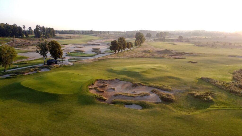 Sólbjartur golfvöllur með sandbyrgjum, grænum brautum og vatnshindrun nálægt trjám