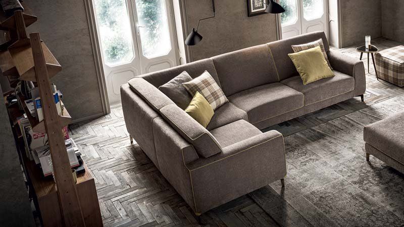 Un grande divano componibile è posizionato in un soggiorno, accanto a una finestra.