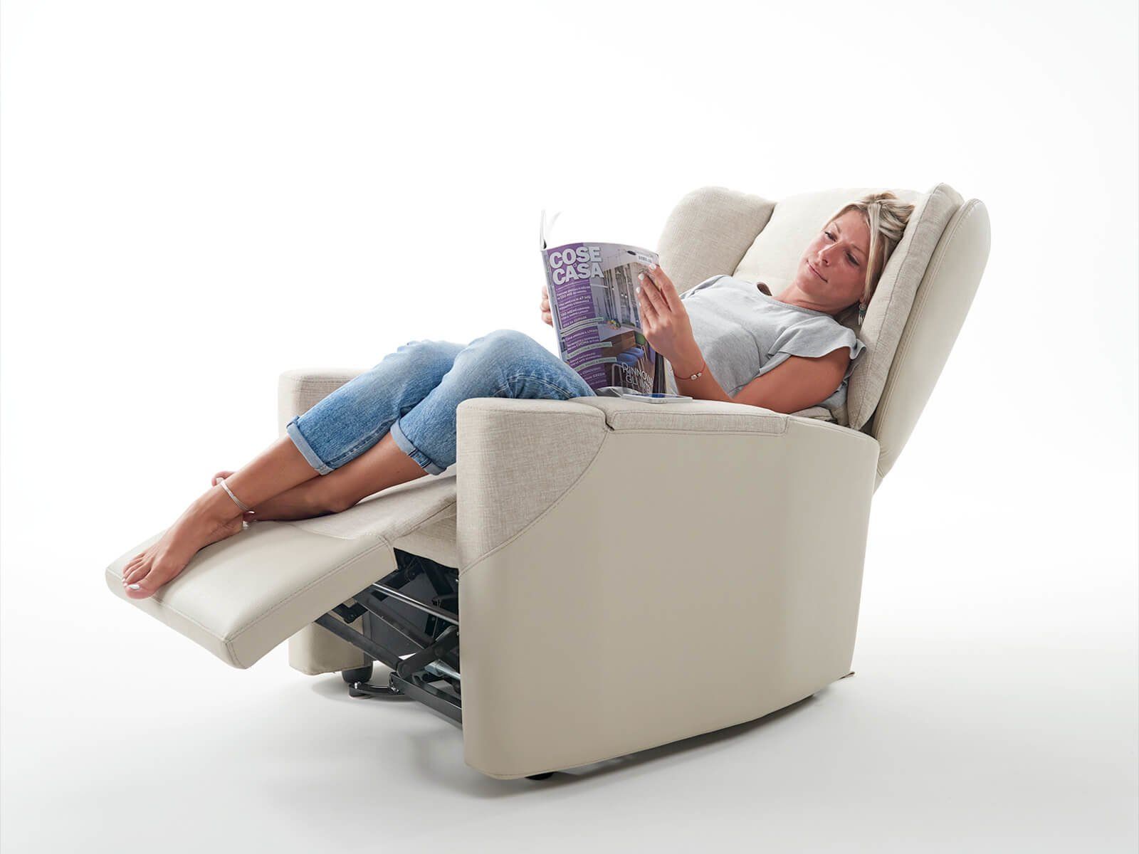 Una donna è seduta su una poltrona reclinabile e legge una rivista.