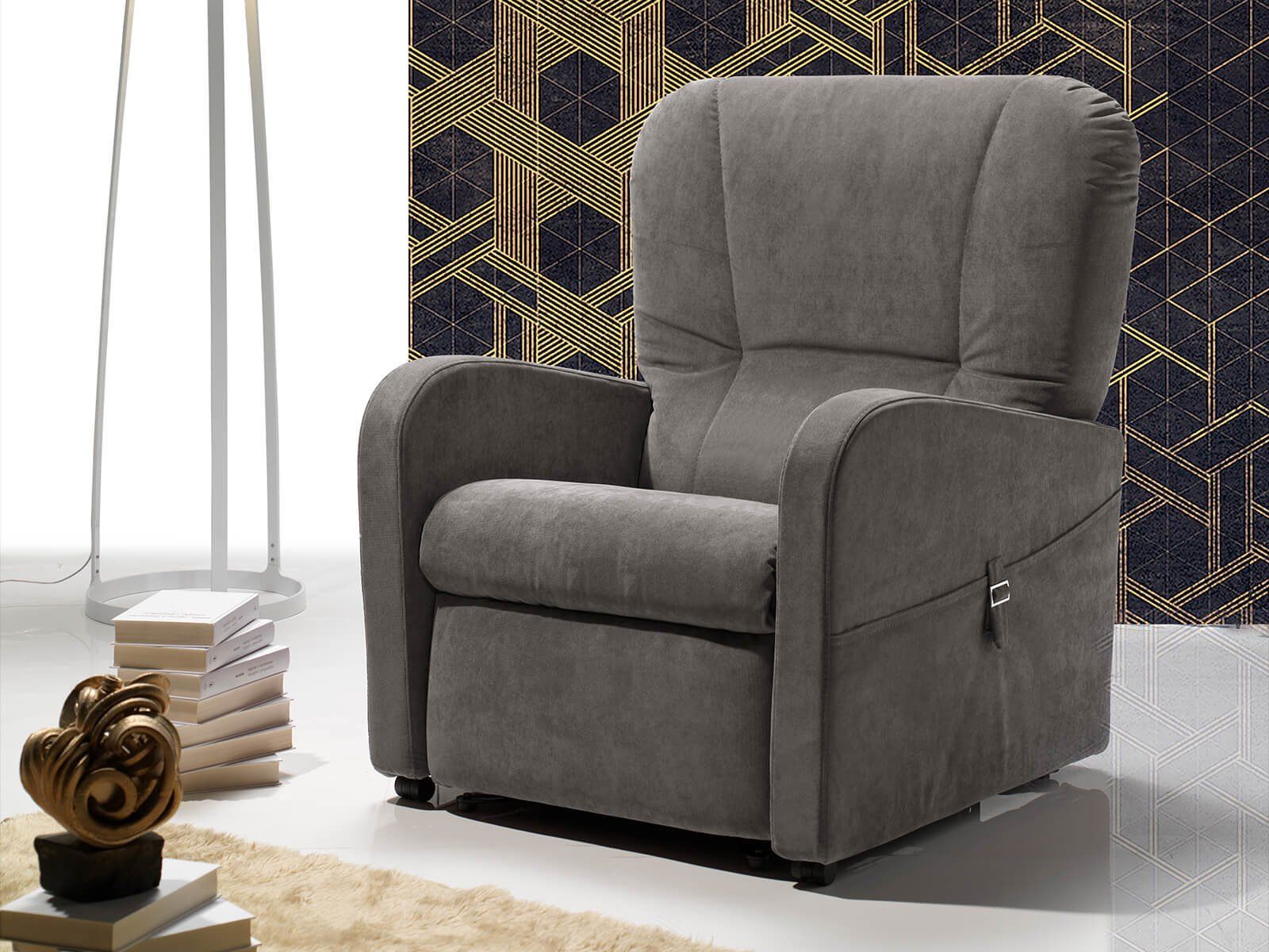 Una poltrona reclinabile grigia è posizionata in soggiorno accanto a una lampada e a dei libri.