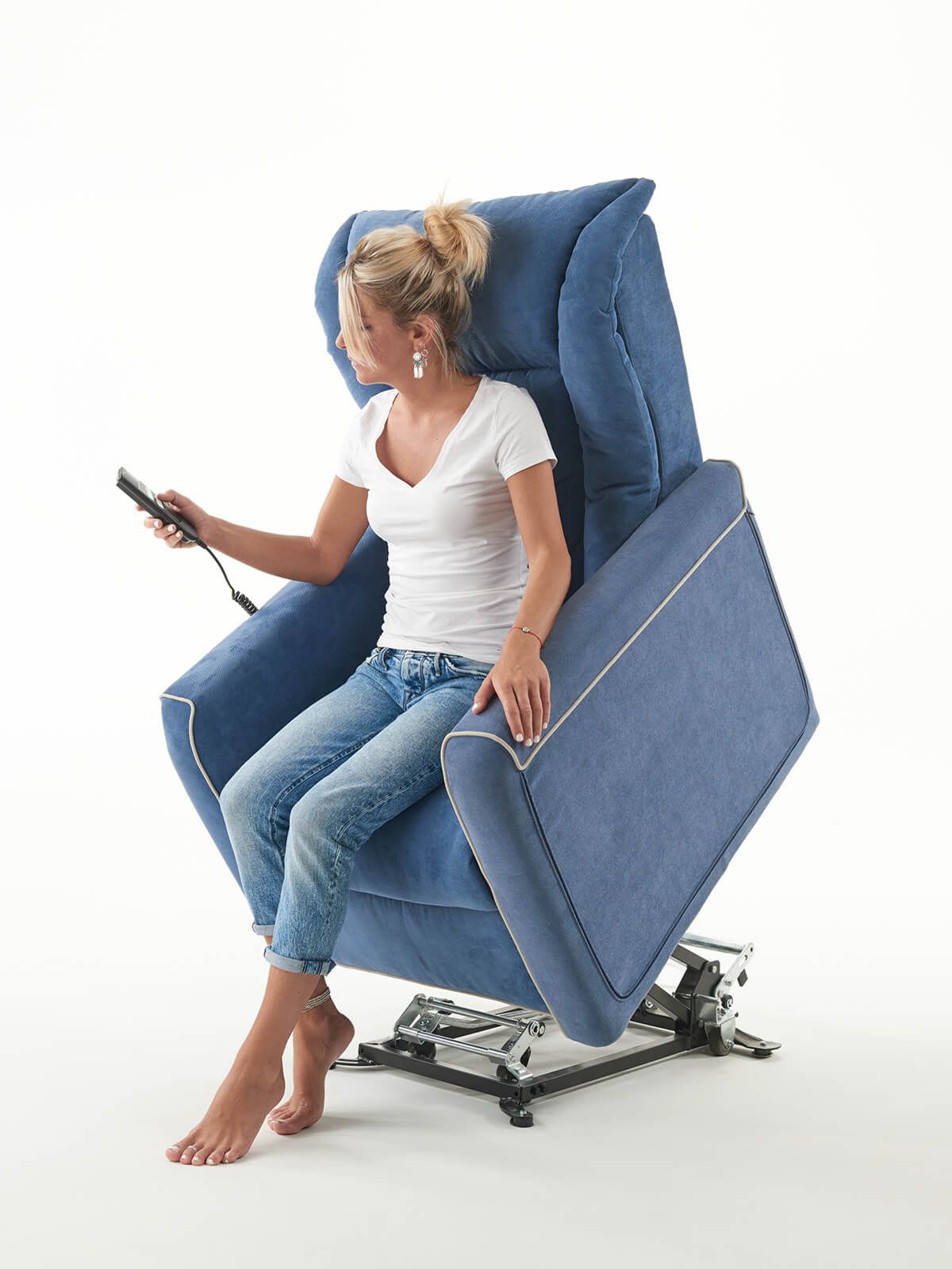 Una donna è seduta su una sedia blu e tiene in mano un telecomando