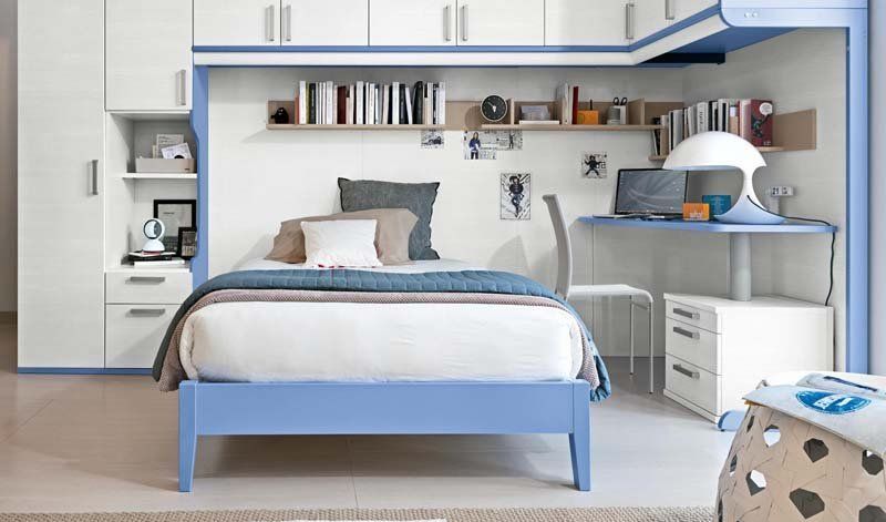 Una camera da letto con un letto blu, armadi bianchi e una scrivania.