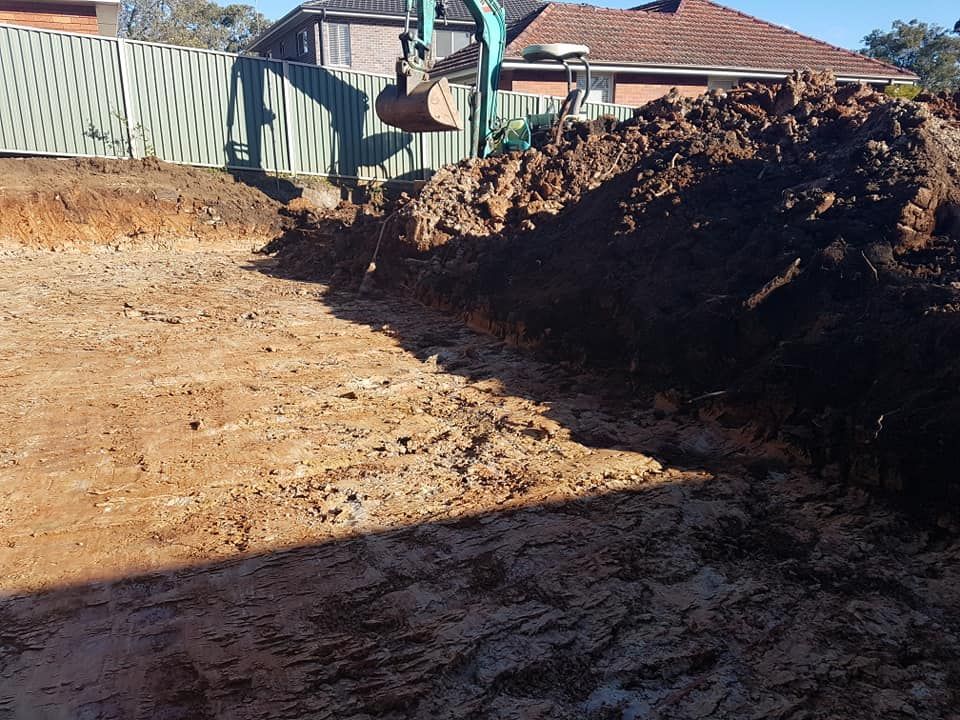 An excavator is digging a hole in the dirt in front of a house