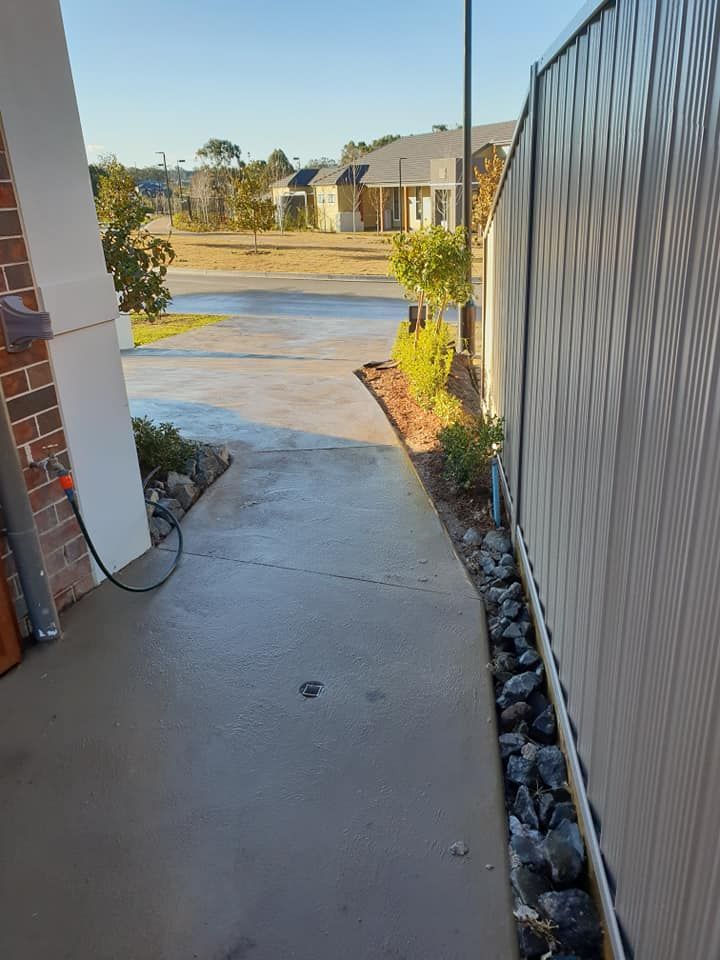 A sidewalk next to a fence with a hose attached to it.