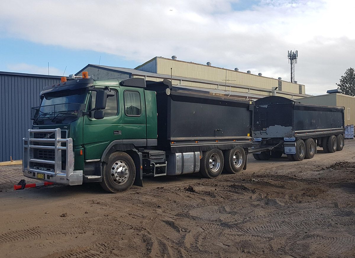 A green dump truck is parked in a dirt lot next to a building.